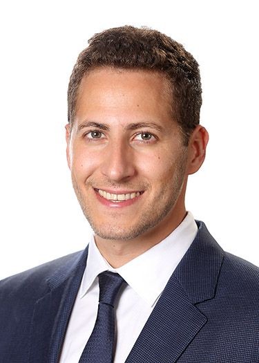 Person in a blue suit and white shirt with a black tie, posed against a white background.